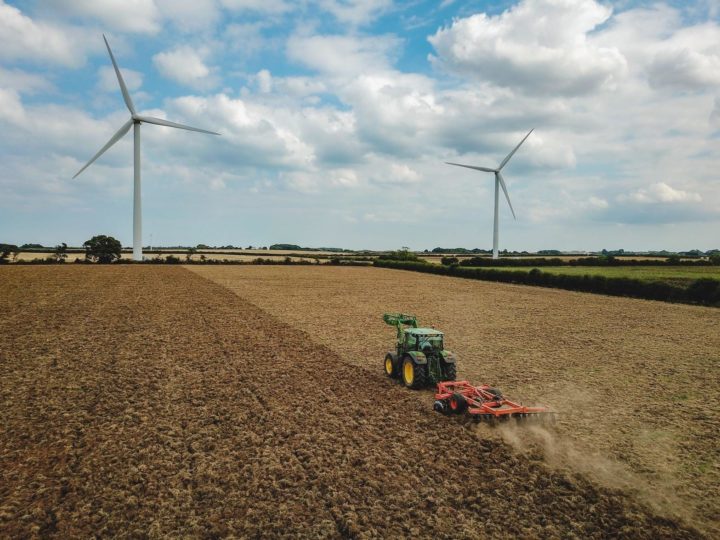 Wind turbines on farm with tractor ploughing the field.